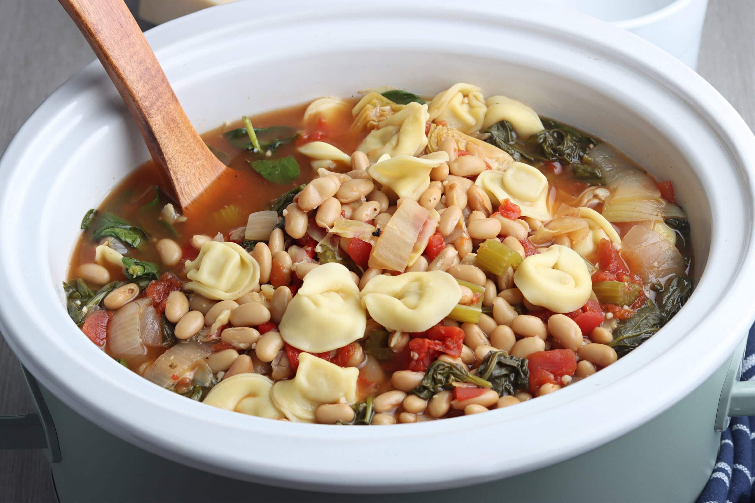 tortellini soup ingredients in slow cooker with wooden spoon