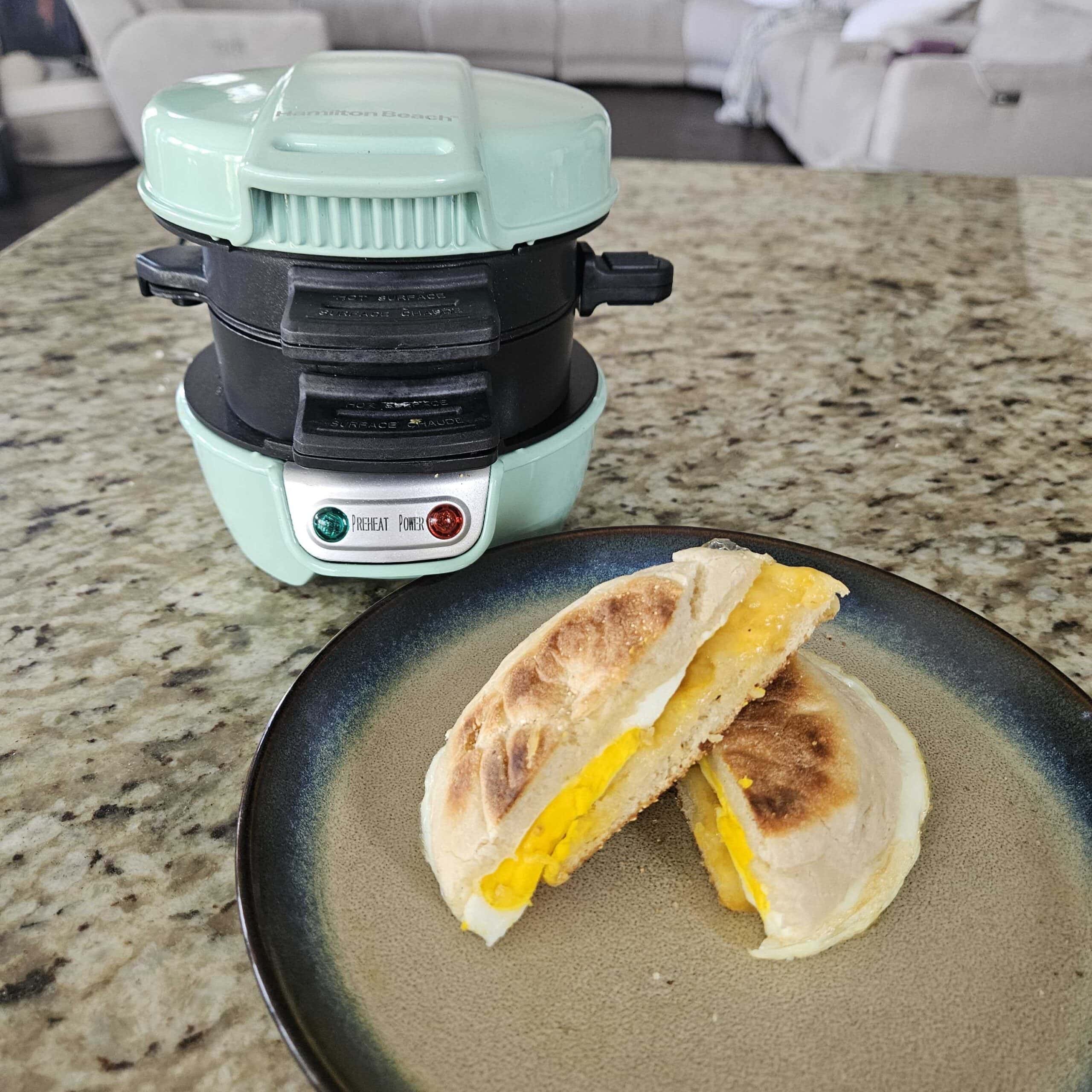 hamilton beach sandwich maker in blue with breakfast sandwich on plate