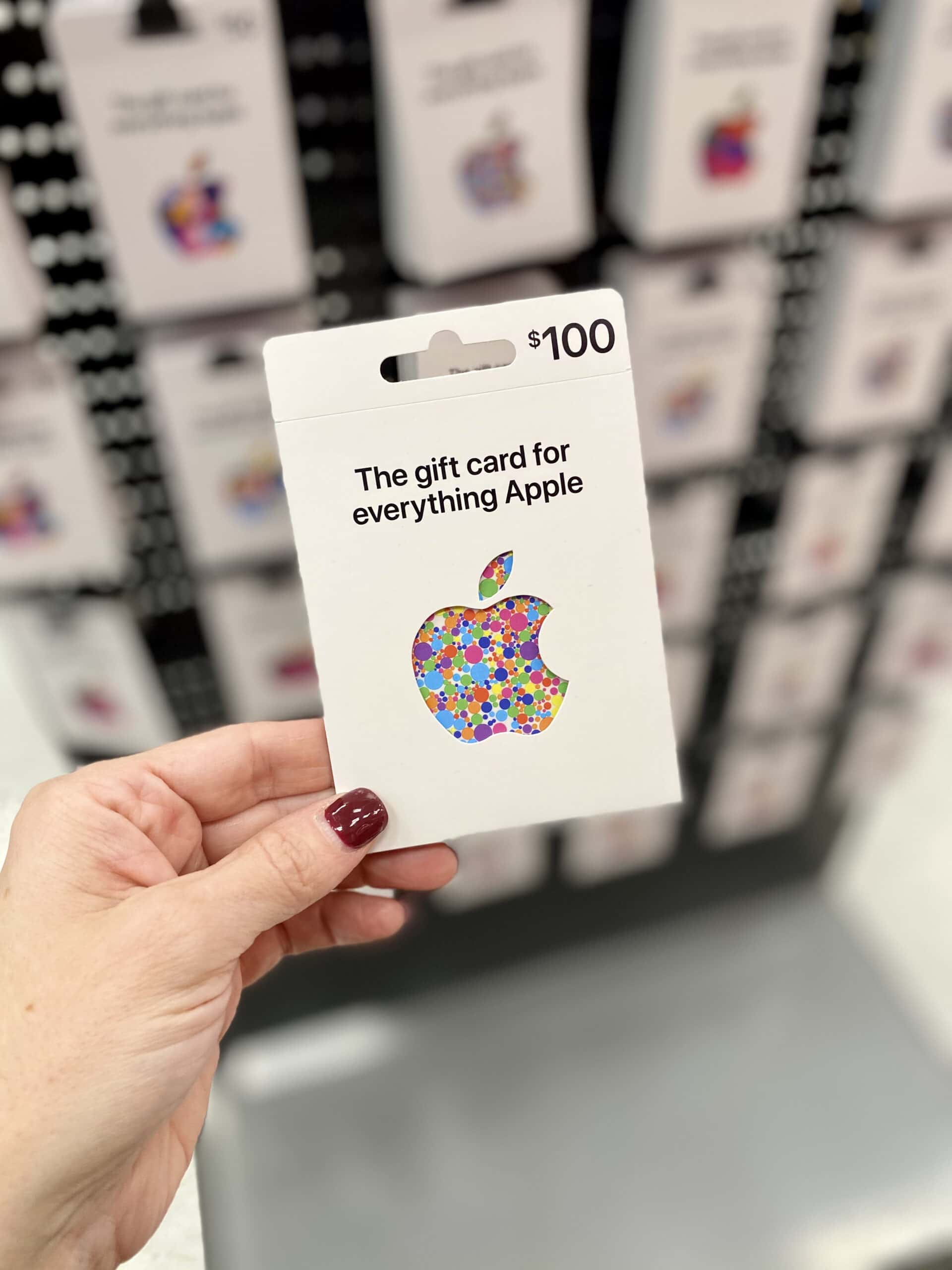 apple $100 gift card being held in front of display in womans hands with red nails