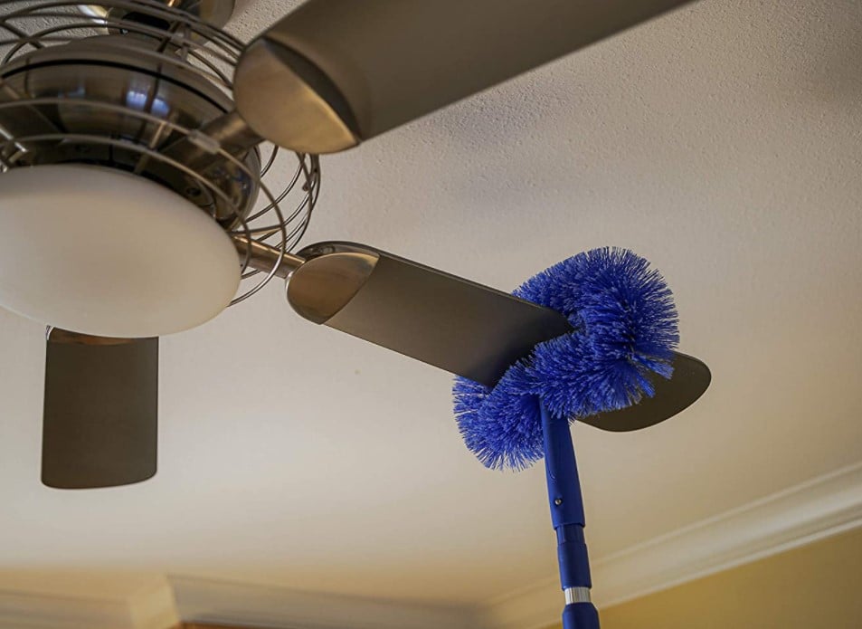 using a brush on a ceiling fan blade to clean it 