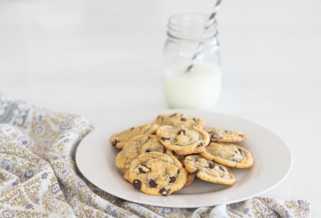 Chocolate chip cookies on a plate with a glass of milk with a straw