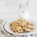Chocolate chip cookies on a plate with a glass of milk with a straw