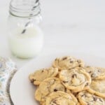 Chocolate chip cookies on a plate with a glass of milk with a straw