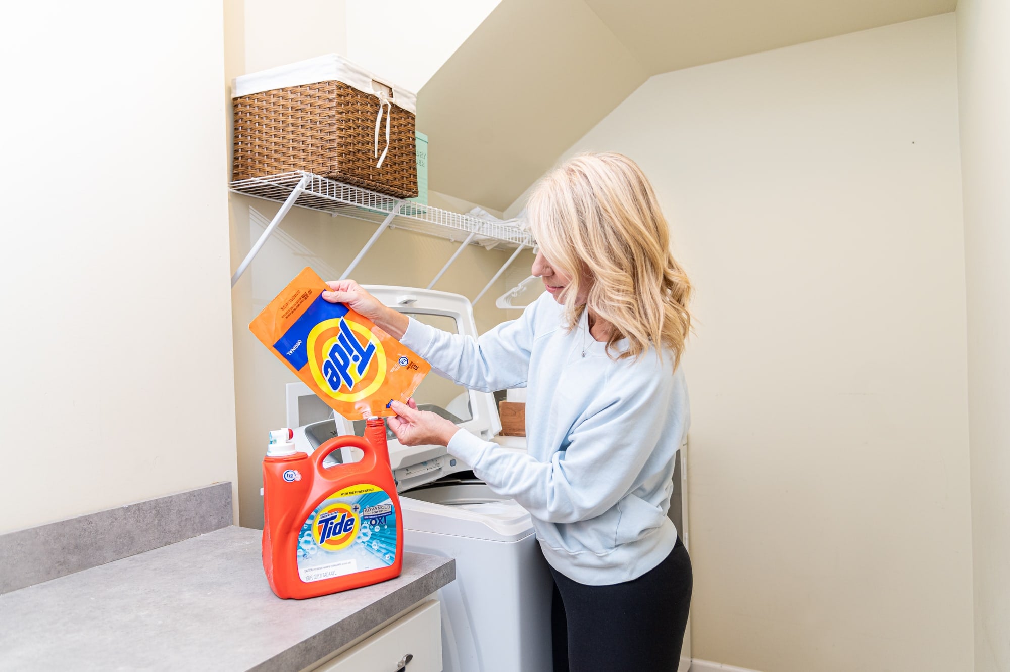 Laurie pouring Tide refill in bottle in laundry room