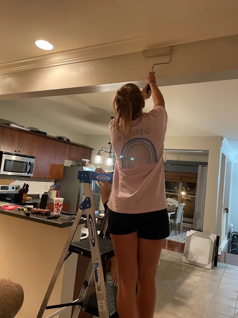 person painting near a kitchen using paint roller standing on ladder 
