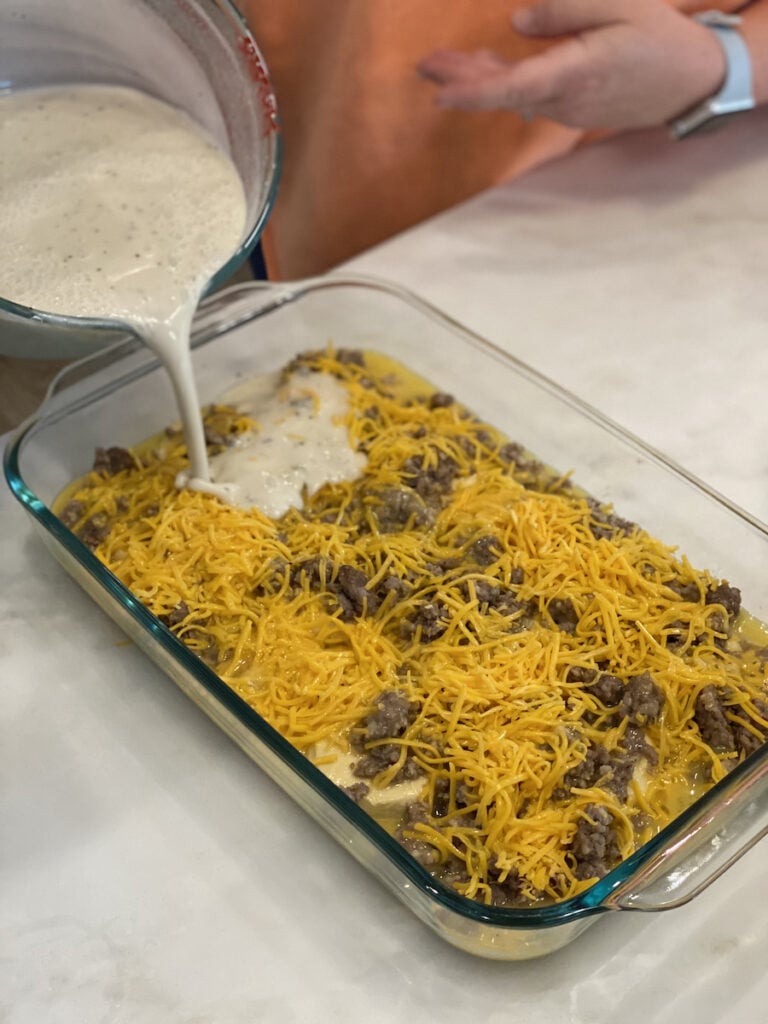 pouring gravy over biscuits and gravy casserole