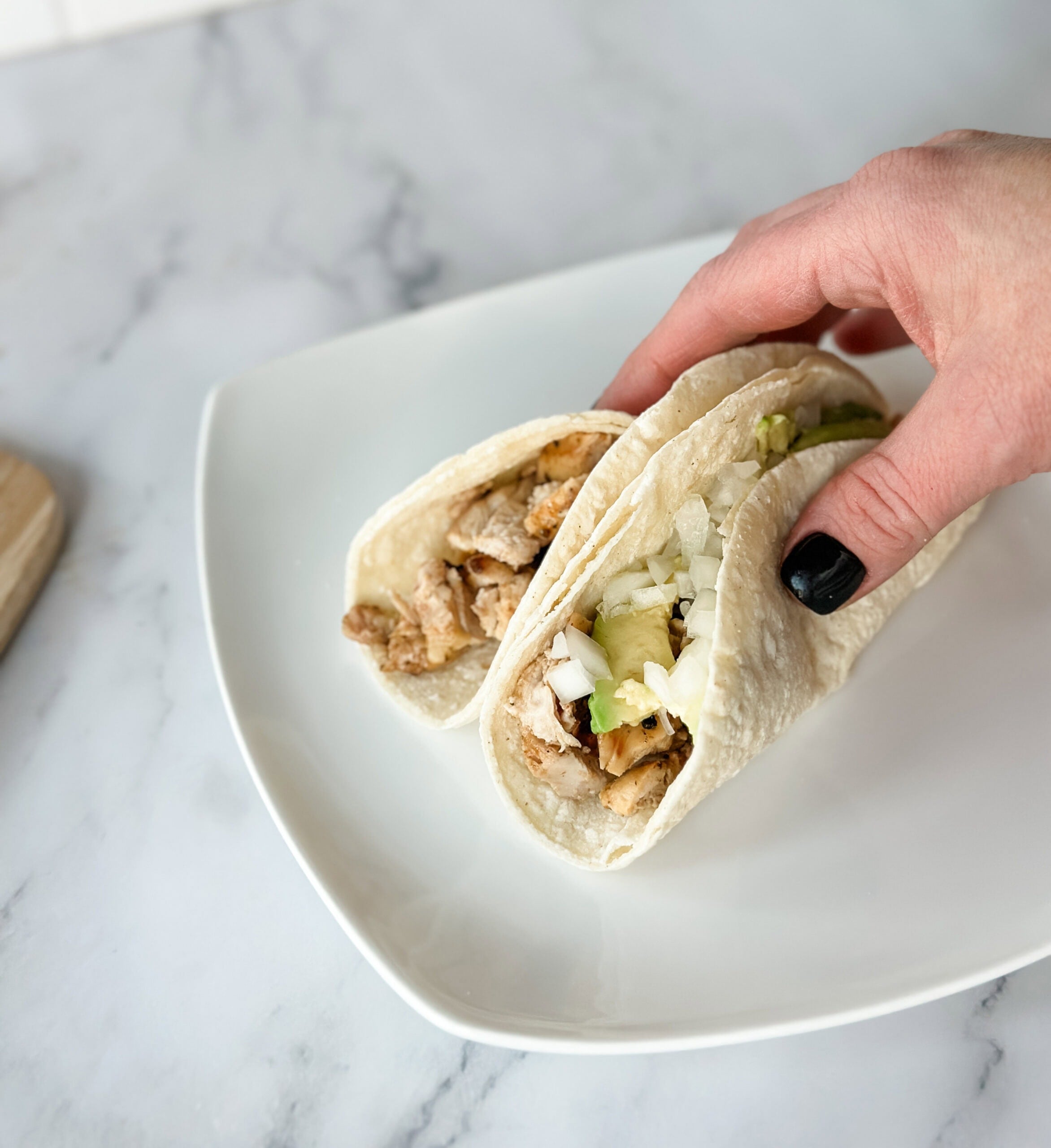 Chicken street tacos in hand with plate 