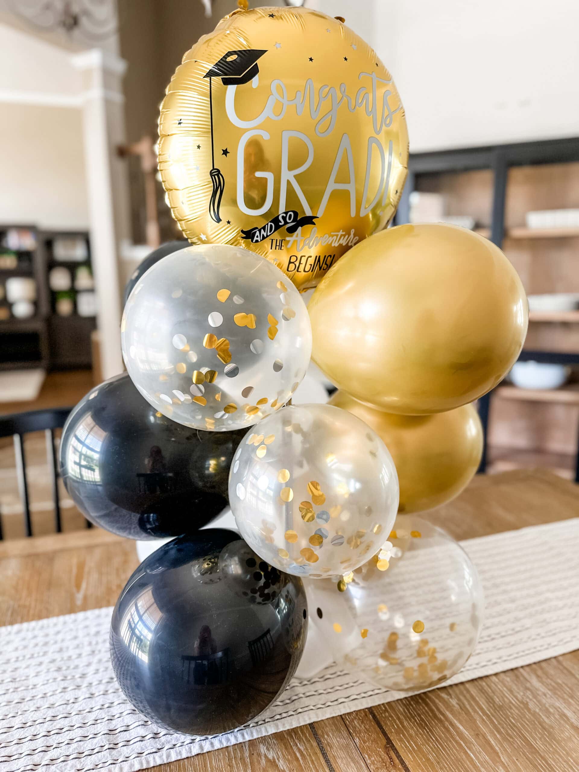 finished diy balloon bouquet with black, confetti, and gold balloons sitting on a table.
