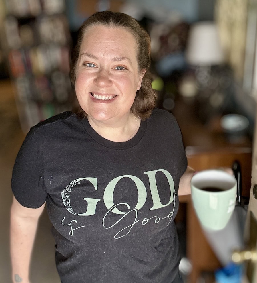 woman wearing a black god is good green text shirt with a teal coffee cup