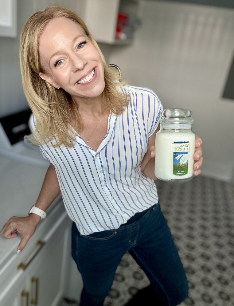 yankee candle clean cotton candle held in hand by woman in a laundry room wearing a striped shirt 