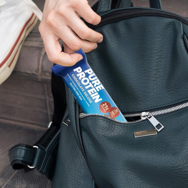 person putting pure protein bar in backpack